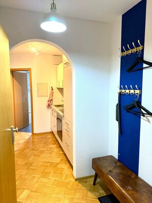 A hallway with a wooden floor, a bench, a coat rack, and a kitchen area with cabinets and a sink. - VetterLux Lumi - Balcony, Parking, Greenery view (Ravensburg)