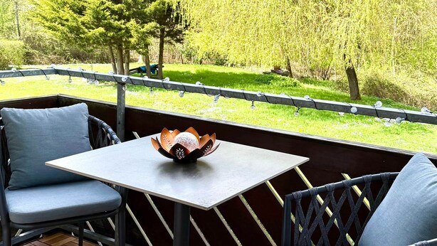 Une terrasse extérieure avec une table et deux chaises, un bol décoratif posé sur la table, et une vue sur un paysage verdoyant avec des arbres.