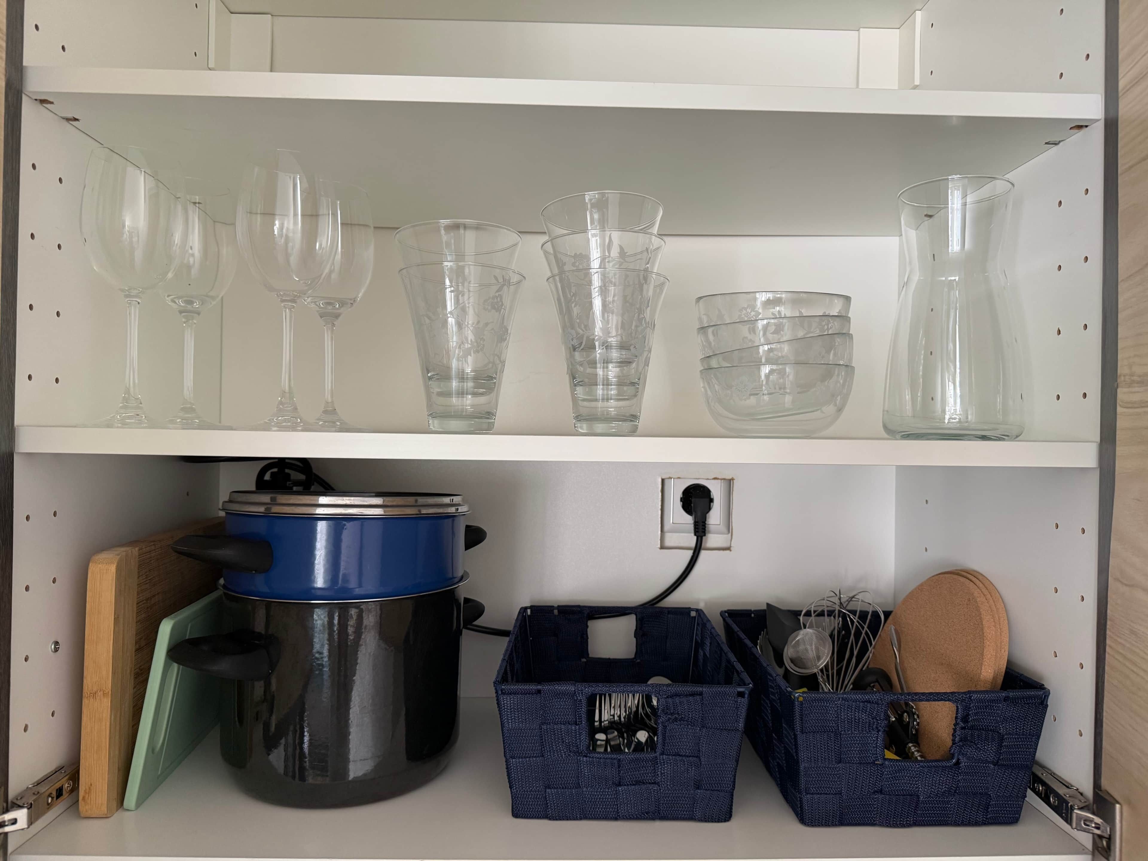A kitchen shelf with various glassware and a blue pot.