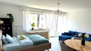 A modern hotel room with a bed, a round wooden table, a blue sofa, and a window with curtains. - VetterLux Nova - bright, quiet & central (Ravensburg)