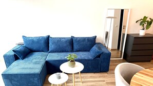 A modern living room with a blue sectional sofa, two small white tables, a wooden chair, and a potted plant. - VetterLux Nova - bright, quiet & central (Ravensburg)