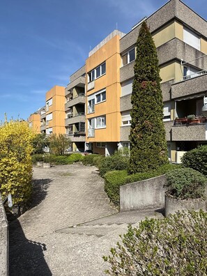 A multi-story residential building with balconies, a paved pathway, and surrounding greenery.