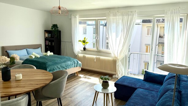 A modern bedroom with a bed, bedside table, chair, and a view of the city. - VetterLux Nova - bright, quiet & central (Ravensburg)