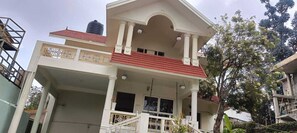 A two-story building with a balcony, a water tank on the roof, and a tree in the background.