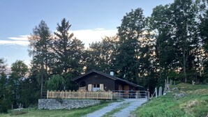 Une cabane en bois avec une entrée en pierre, entourée d’arbres et bordée d’un chemin de gravier.