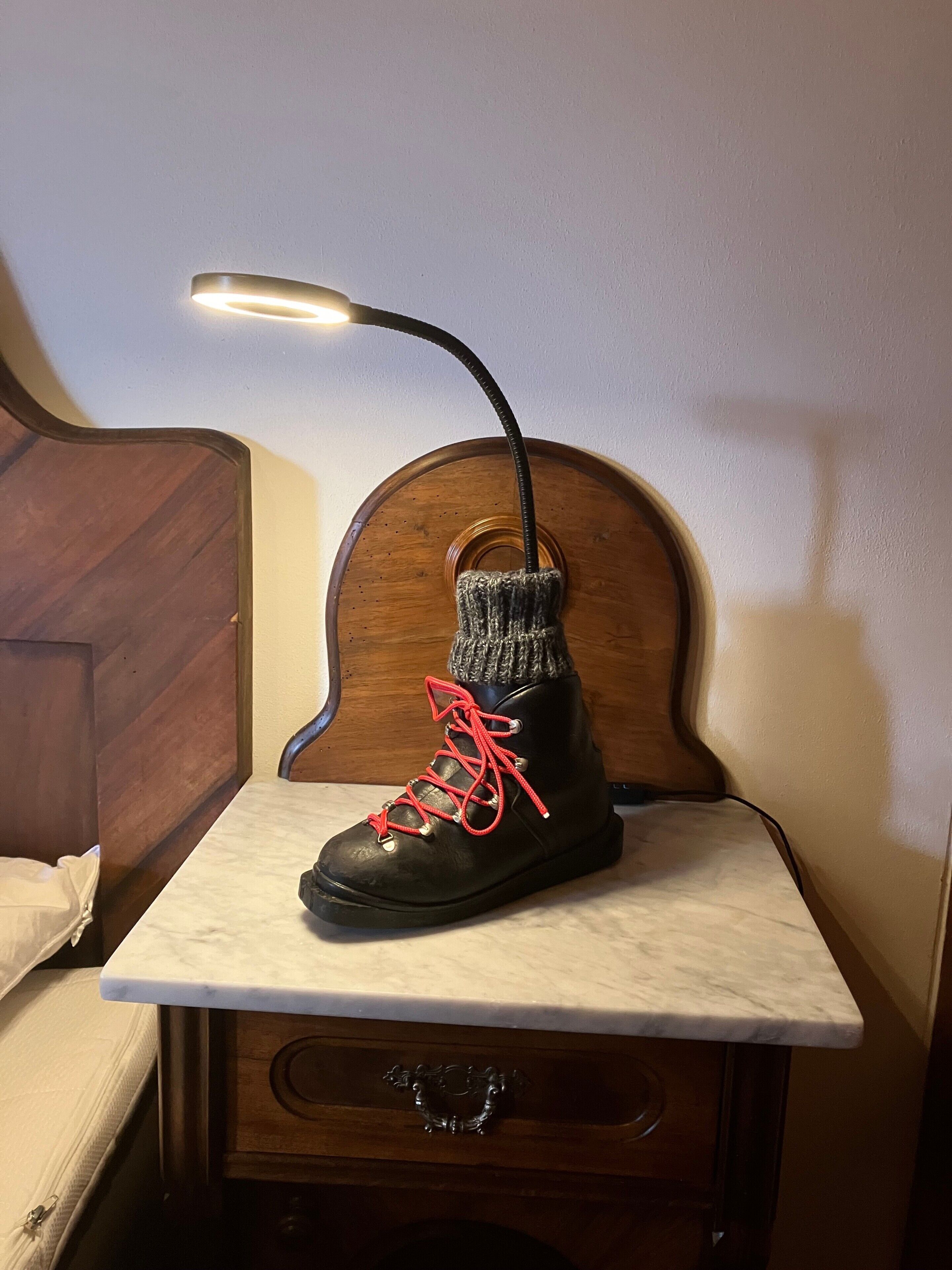 Una bota negra con cordones rojos sobre una mesita de noche con un cajón.