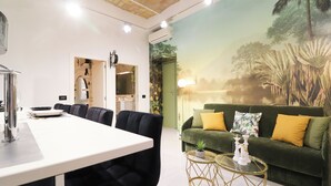 Ein modernes Wohnzimmer mit einem grünen Sofa, einem Essbereich mit einem weißen Tisch und einem Wandbild mit einer tropischen Szene.