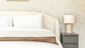 Una cama bien hecha con sábanas blancas, una lámpara de noche y una mesita de noche con cajones.