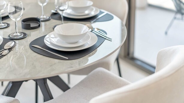Una mesa redonda de comedor con un tablero de mármol blanco, manteles individuales negros, platos blancos y cubiertos.