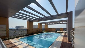 Piscina en la azotea con pérgola, terraza de madera y vista a la ciudad.