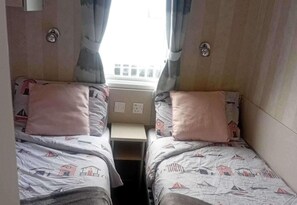 A small, narrow room with two beds, each with a pillow and a patterned bedspread. - Property (Ayr)