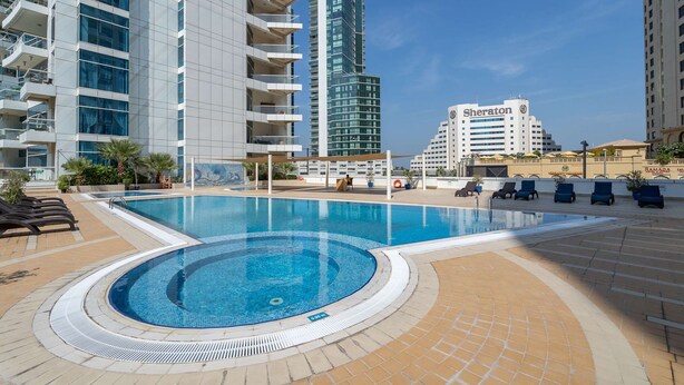 A swimming pool with lounge chairs, a Sheraton hotel, and high-rise buildings in the background. - Free Housekeeping Visits During Your Stay - Stayshort - Elegant 2 Bedroom in Dubai Marina That Sleeps 4 (Dubai)