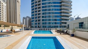 A rooftop swimming pool with lounge chairs and a lifebuoy, surrounded by high-rise buildings. - Free Housekeeping Visits During Your Stay - Stayshort - Elegant 2 Bedroom in Dubai Marina That Sleeps 4 (Dubai)