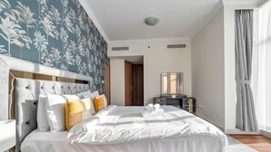 A hotel room with a large bed, a headboard, a nightstand, a mirror, and a window with curtains. - Free Housekeeping Visits During Your Stay - Stayshort - Elegant 2 Bedroom in Dubai Marina That Sleeps 4 (Dubai)