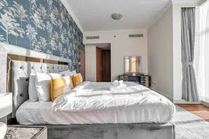 Ein Hotelzimmer mit einem großen Bett, einem Kopfteil, einem Nachttisch, einem Spiegel und einem Fenster mit Vorhängen.