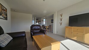 A living room with a sofa, a coffee table, a TV on a wooden cabinet, and a dining area in the background. - Edinburgh 1BR Apt with Balcony & Lift (Edinburgh)
