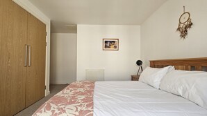 A bedroom with a bed, a wardrobe, a radiator, a framed picture, and a dreamcatcher. - Edinburgh 1BR Apt with Balcony & Lift (Edinburgh)