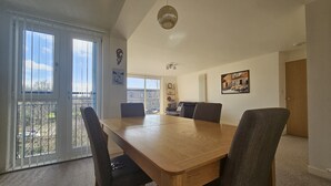 A dining area with a wooden table and chairs, large windows, and a view of the outdoors. - Edinburgh 1BR Apt with Balcony & Lift (Edinburgh)