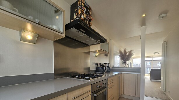 A modern kitchen with a gas stove, oven, and coffee maker. - Edinburgh 1BR Apt with Balcony & Lift (Edinburgh)