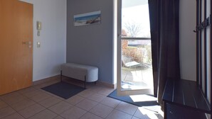 Una habitación con un banco, una puerta, un teléfono, un cuadro y vistas a través de un ventanal.