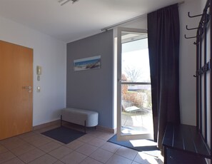 Ein Zimmer mit einer Sitzbank, einer Tür, einem Telefon, einem Gemälde und Blick durch eine Glastür.