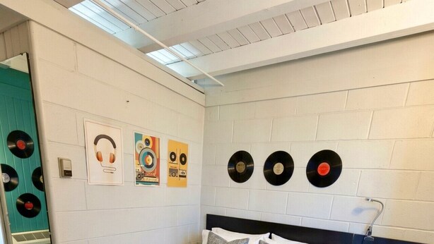 A bedroom with a bed, pillows, a bedside table, and wall decorations including vinyl records. - The Vinyl Lounge at The Cedar (Sandusky)