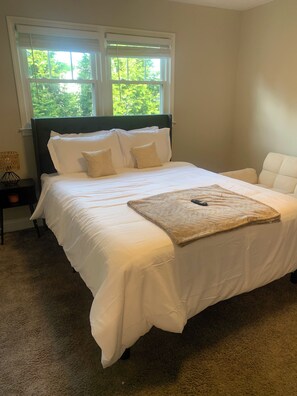 A neatly made bed with white linens, a headboard, and a window with blinds. - Just Visiting!! (Charlotte)