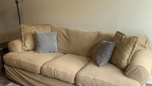 Un sofá color beige con tela texturizada, una alfombra gris y un cuadro colgado en la pared con flores.