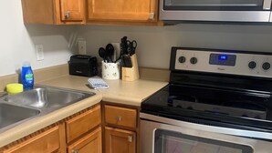 Una cocina con armarios de madera, un microondas de acero inoxidable, un tostador y un horno negro.
