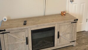 Una habitación con un televisor montado en la pared, un mueble de madera con cajones y una puerta.