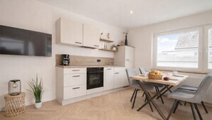 Una cocina moderna con armarios blancos, horno empotrado y un comedor con mesa y sillas.