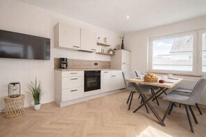 A modern kitchen with white cabinets, a built-in oven, and a dining area with a table and chairs. - Apartment Inselzeit No. 1 on Borkum - with terrace, WLAN and private parking space (Borkum)