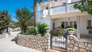A two-story building with a stone wall, a gate, and potted plants. - Studio apartment Luce (Povljana)