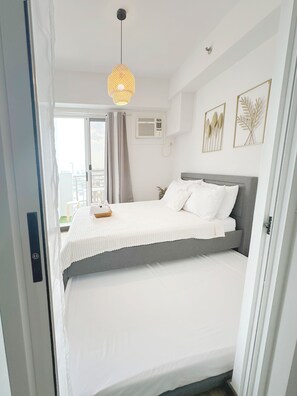 A double bed with white bedding, a grey headboard, a woven pendant light, and two framed wall art pieces.
