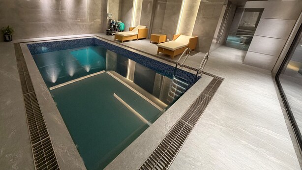 En moderne indendørs pool med blå mosaikdetaljer, liggestole og et spa-område.