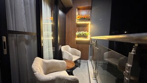 Et moderne interiør med gelænder af glas, to lænestole, et lille bord og en trævæg med en hængende plante.