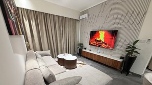 En moderne stue med et stort fladskærms-tv, en beige modulsofa, to runde sofaborde og en potteplante.