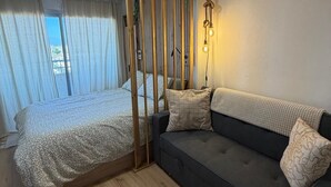 Una stanza con un letto, un divano, un pannello in legno, una luce a soffitto e vista dalla finestra.