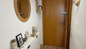 Un corridoio con una porta in legno, una consolle bianca con oggetti decorativi, uno specchio rotondo e luci a parete.