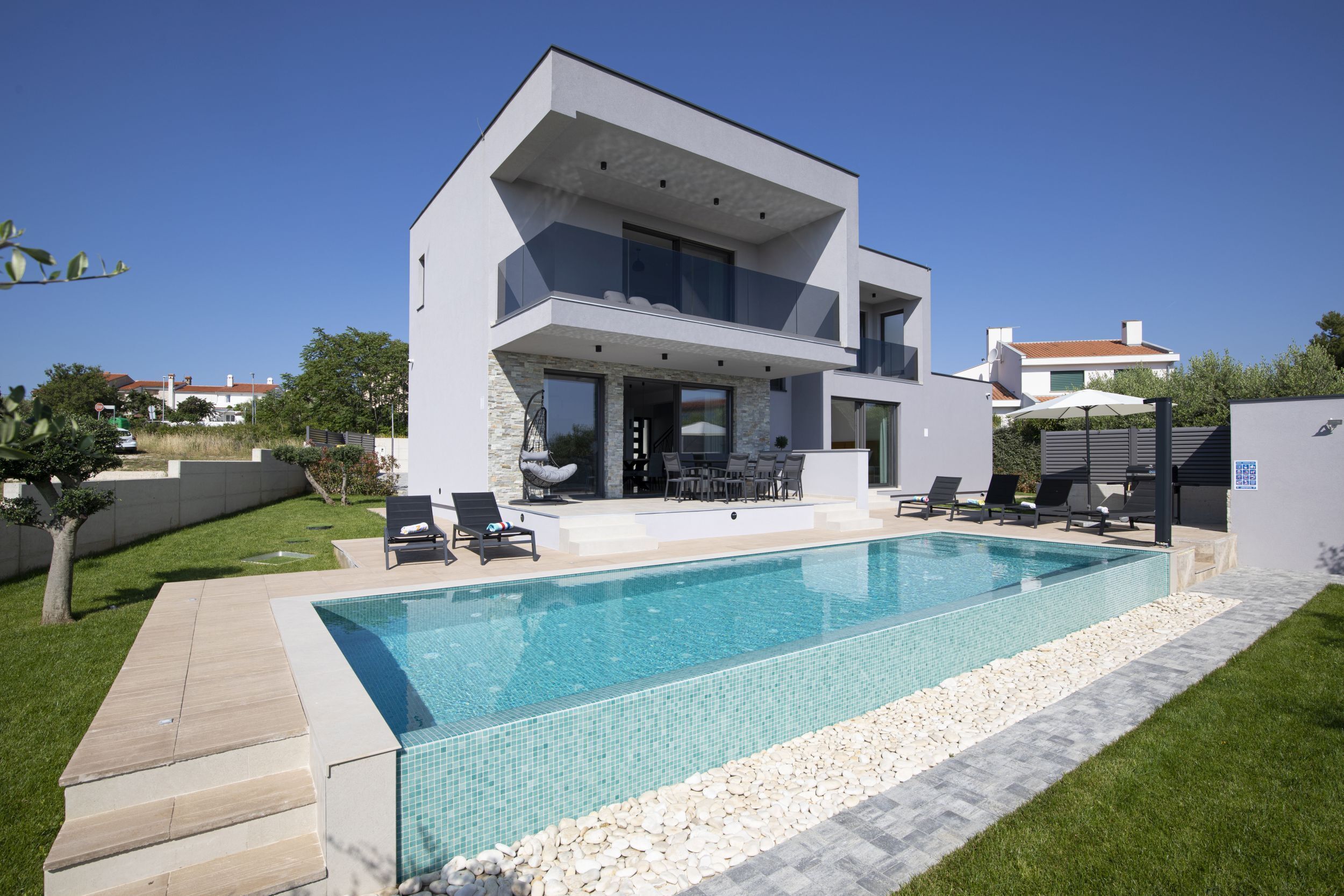 A modern two-story house with a swimming pool, outdoor seating, and a view of the neighborhood.
