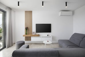A modern living room with a grey sofa, a white coffee table, a TV on a white cabinet, and a large window with curtains. - Villa Leola in Ližnjan (Ližnjan)