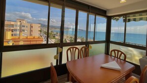 Ein Zimmer mit großem Fenster und Blick auf die Küste, einem Holztisch und Stühlen.