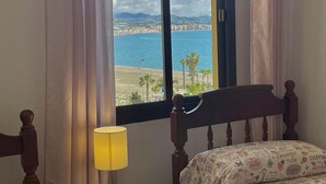 Ein Schlafzimmer mit Blick auf Strand und Stadtlandschaft durch ein großes Fenster.