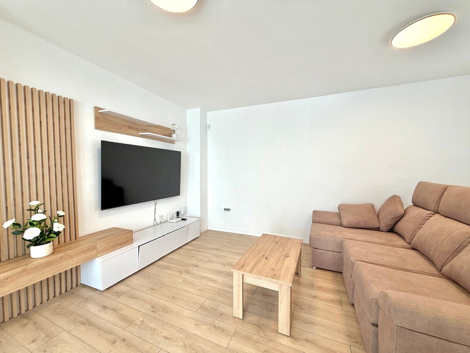 Una sala de estar moderna con televisor de pantalla plana, panel de pared de madera, sofá color beige y una mesa de centro de madera.