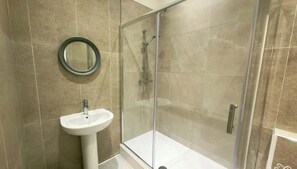 Ein Badezimmer mit einer Duschkabine, einem Standwaschbecken und einem runden Spiegel.
