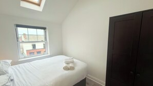 Een slaapkamer met een enkel bed, een raam en een donkere inbouwkast.