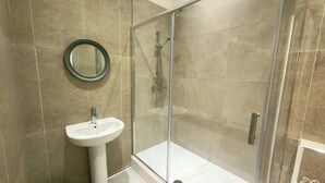 Een badkamer met een douchecabine, een wastafel op een voetstuk en een ronde spiegel.