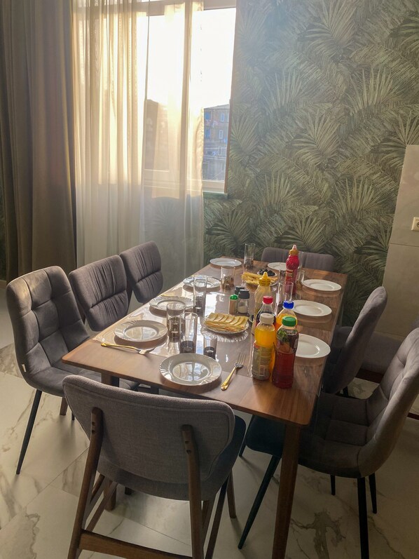 A dining area with a table set for four, chairs, and a window with curtains.