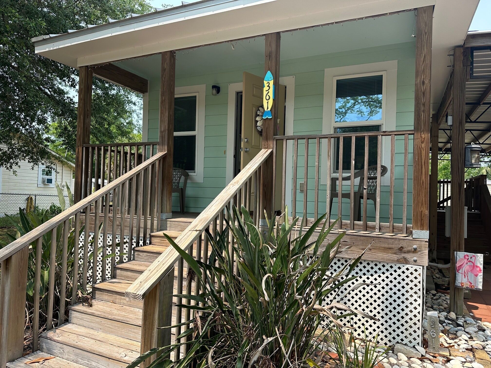 A wooden staircase leading to a porch with a white lattice fence, a wooden railing, and a number sign indicating the house number.