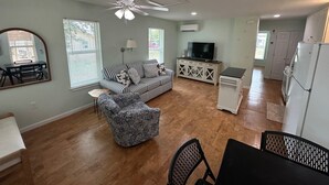 A living room with a sofa, ottoman, and TV, a dining area with a table and chairs, and a kitchen with cabinets and appliances. - Joe's Place- A Hidden Gem by the Bay (Port St Joe)